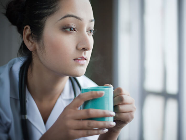 young female doctor with blue mug staring out the window